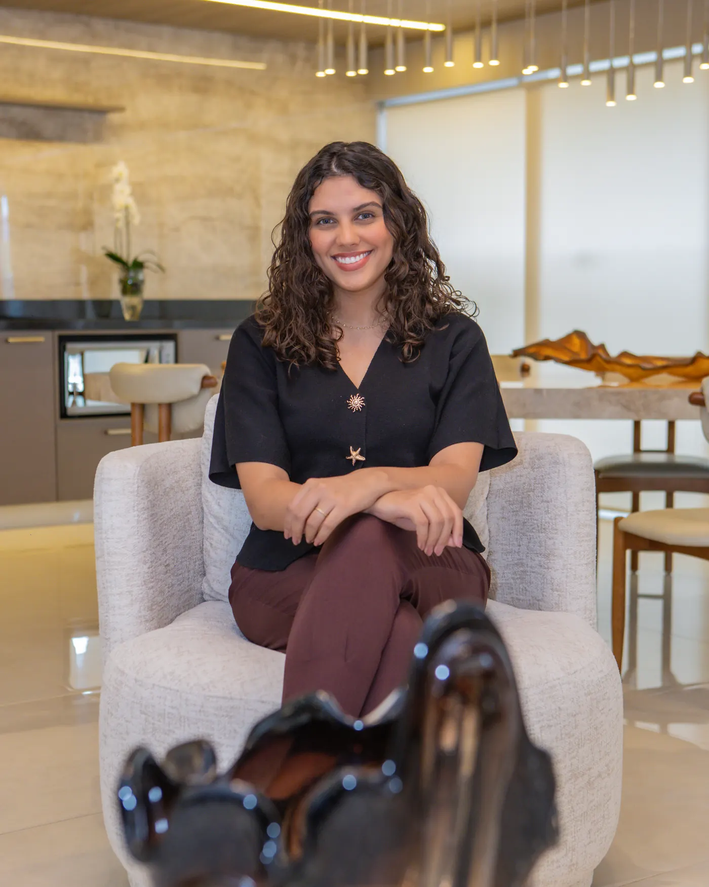 Talyssa Jade sorrindo, sentada em uma poltrona clara no living integrado à cozinha
